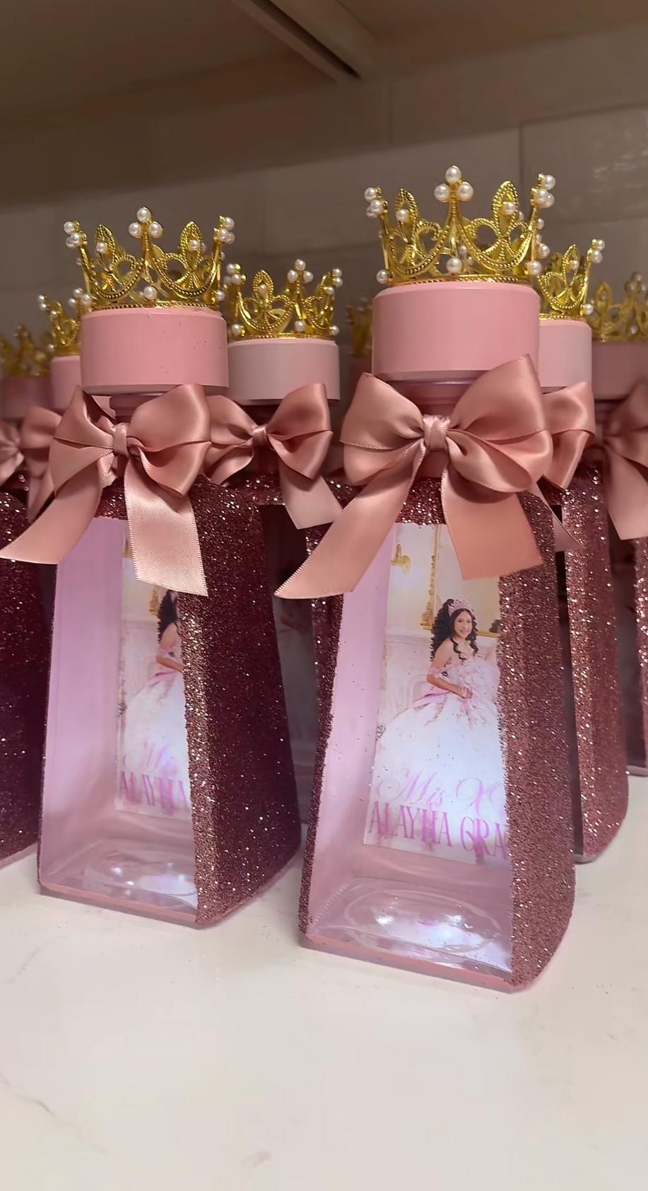 Custom rosegold glitter event favors with gold crown toppers and satin bows, lined up on a white surface