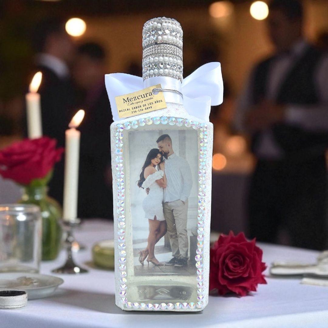Custom white rhinestone bottle with a couple's photo and white satin bow, displayed at a candlelit reception table with red roses