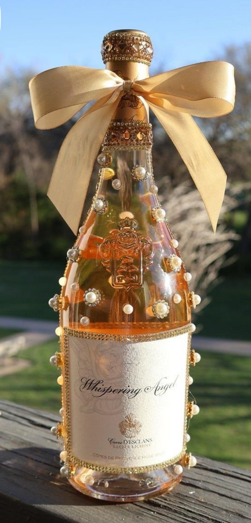 Custom pearl and gold rhinestone bottle decoration with a champagne-gold bow, photographed in natural outdoor light
